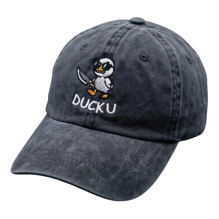 A dark gray washed cotton baseball cap featuring an embroidered cartoon duck character holding a sword and the text 'DUCKU' on the front, displayed on a dark textured surface.